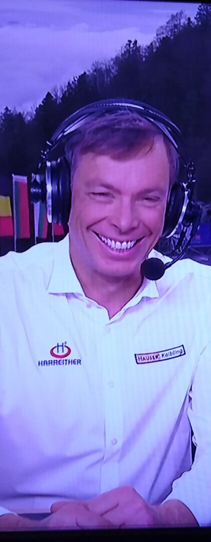 Man smiling wearing a headset and white shirt with logos.